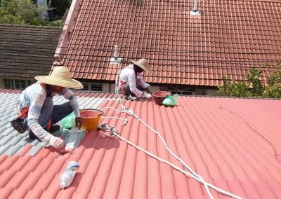 Two skilled workers applying waterproof coating to a clay shingle roof