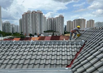 Expert applying waterproof coating to roof tiles with safety gear, in a residential area with high-rise buildings