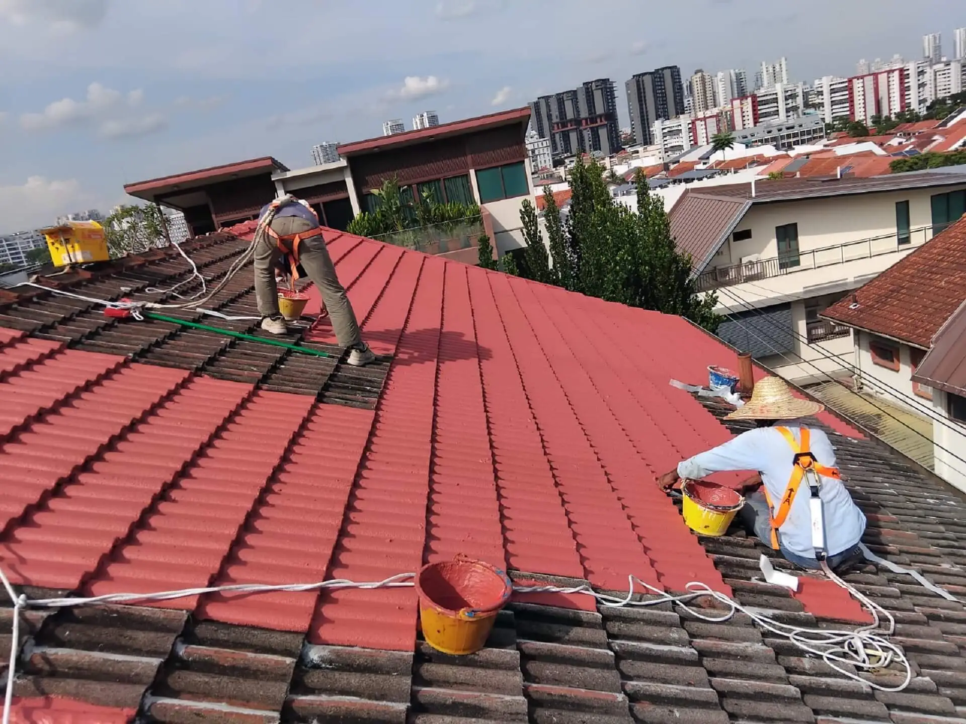 Crane lifting heavy metal roof materials from a red truck and placing them on a rooftop