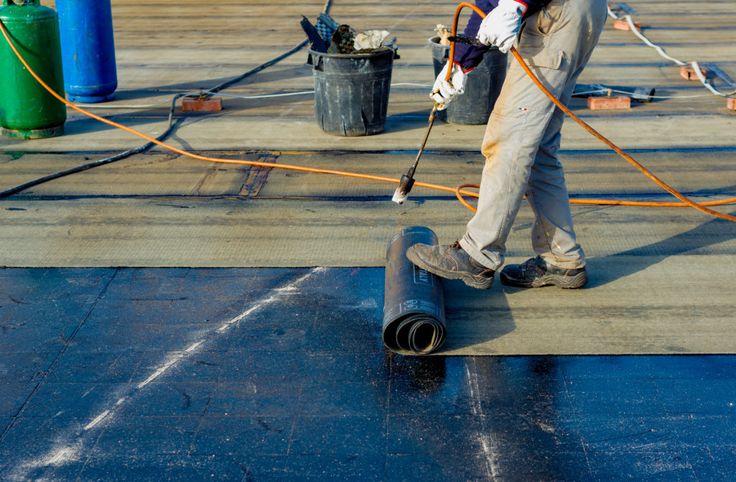 Employee applying sheet membrane waterproof coating on a roof with equipments